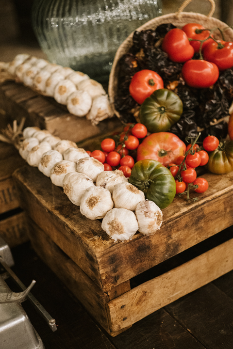 Bodegón con ristras de ajos y tomates en rama sobre cajas de madera.
