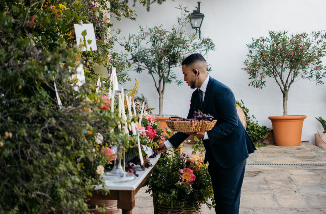 Camarero disponiendo una bandeja de uvas sobre la mesa vestida con flores frescas.